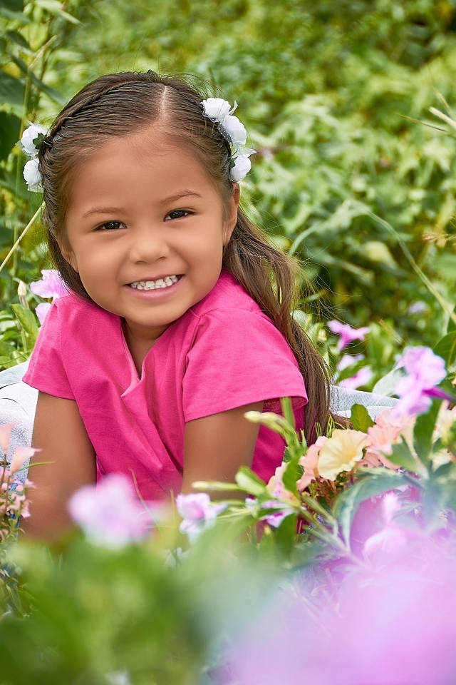 Улыбающаяся маленькая девочка сидит в цветах