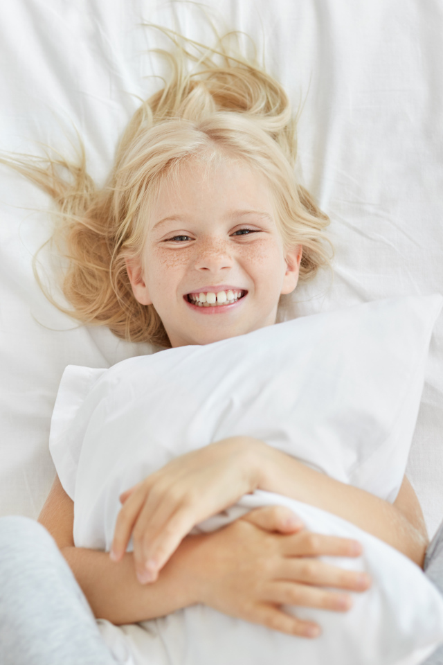 Улыбающаяся маленькая девочка с подушкой на кровати