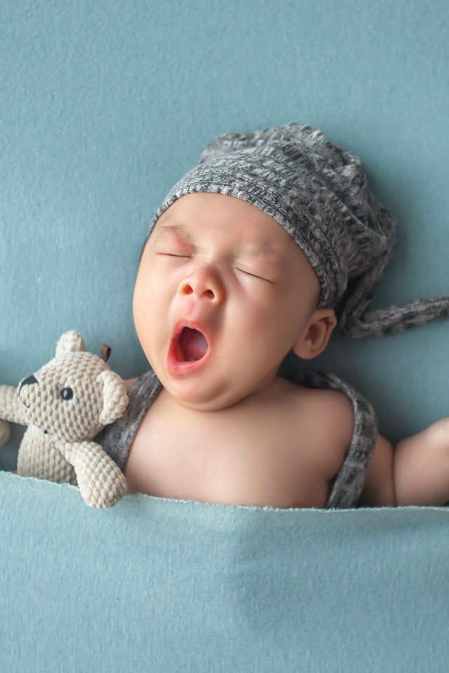 Зевающий малыш с игрушками под серым покрывалом