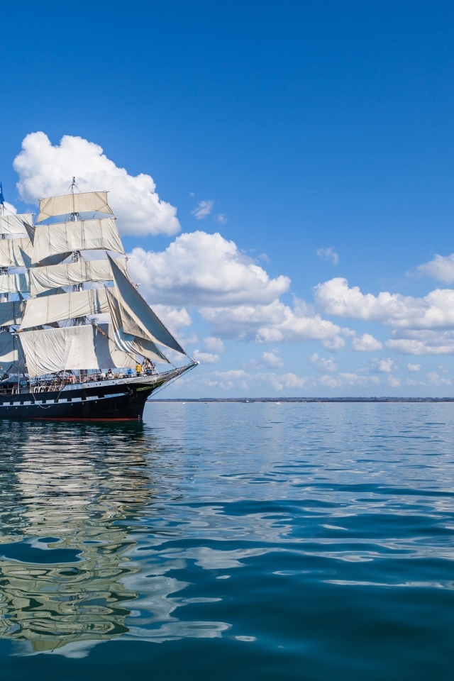 Большой корабль с белыми парусами на фоне голубого неба с облаками в море