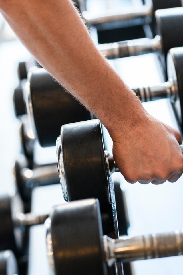 Сильная рука спортсмена берет гантели