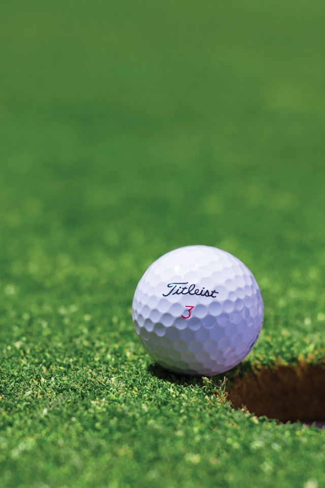 Белый мяч для гольфа лежит у лунки