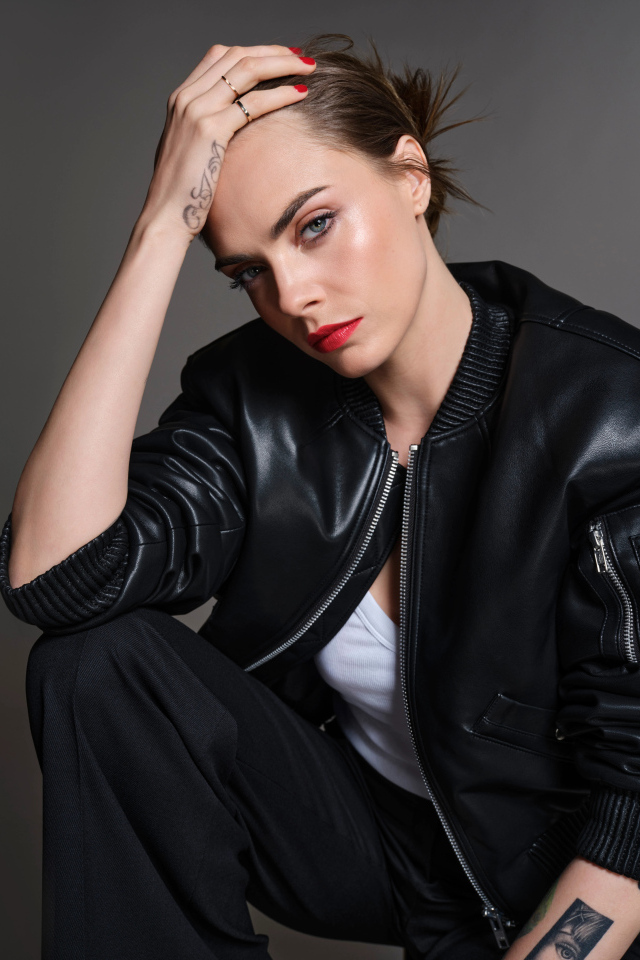 Актриса Кара Делевинь в черной кожаной куртке на сером фоне