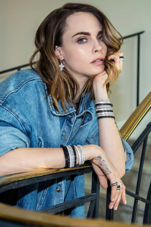 Актриса Кара Делевинь в джинсовой куртке стоит на лестнице