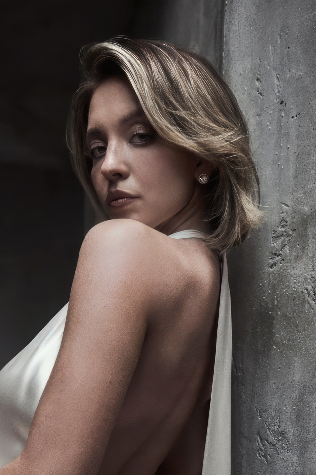 Актриса Сидни Суини стоит у серой стены