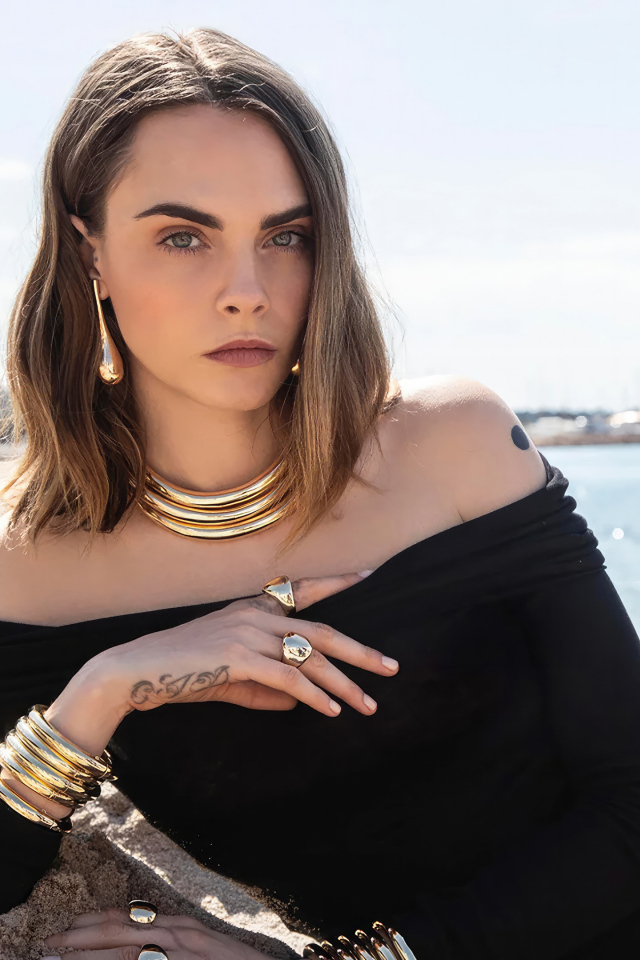 Кара Делевинь в черном платье лежит на песке