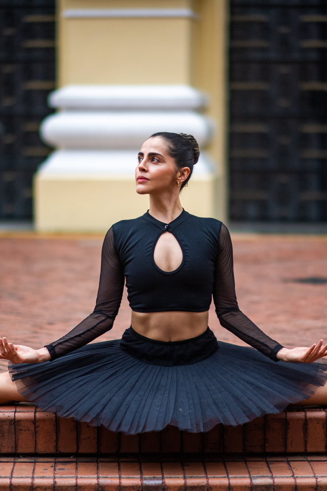 Девушка балерина в черном сидит на шпагате