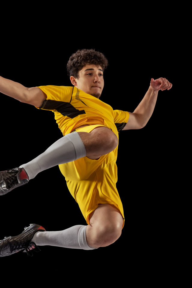 Мужчина футболист отбивает мяч на черном фоне