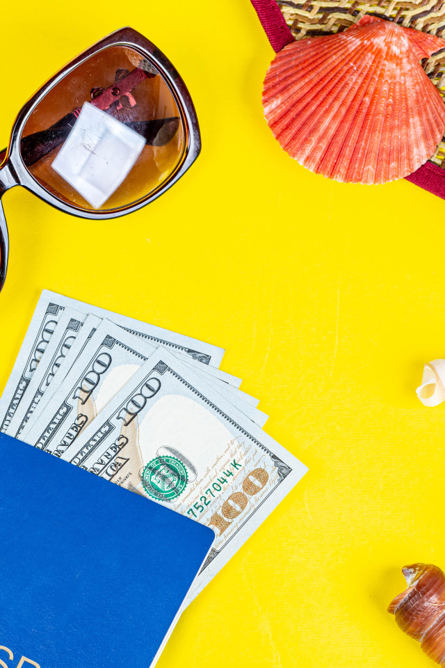 Очки, доллары с паспортом и ракушки на желтом фоне