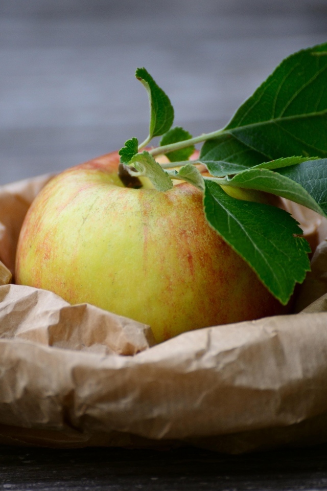 Яблоко с зелеными листьями на бумаге
