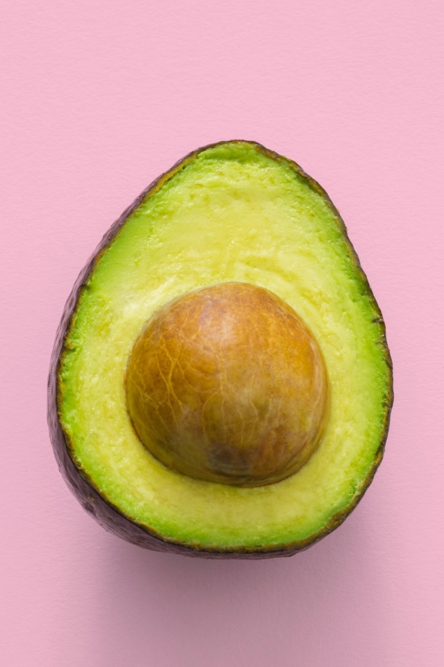 Половина авокадо с большой косточкой на розовом фоне