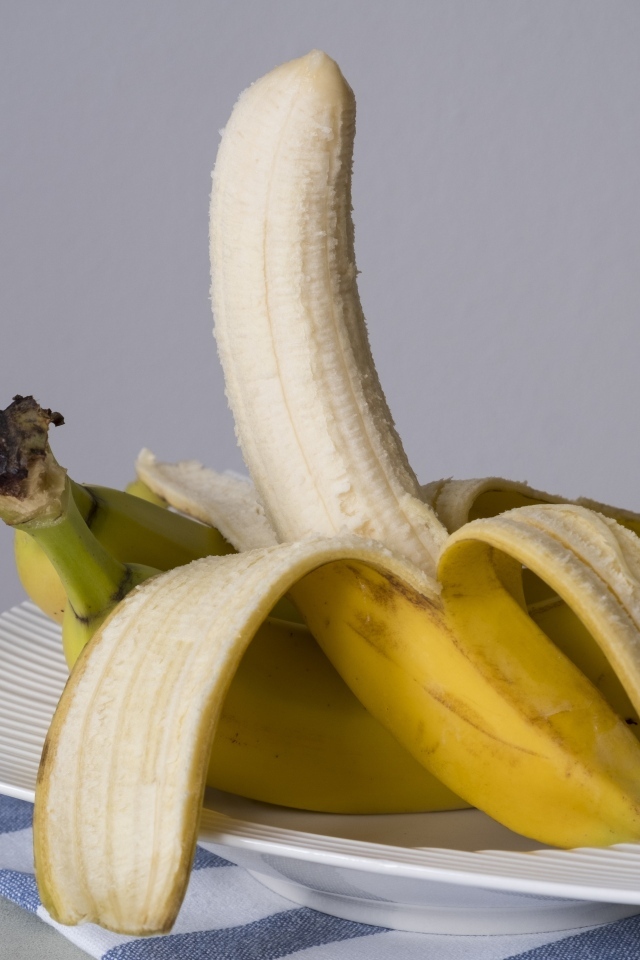 Очищенный банан на тарелке на сером фоне