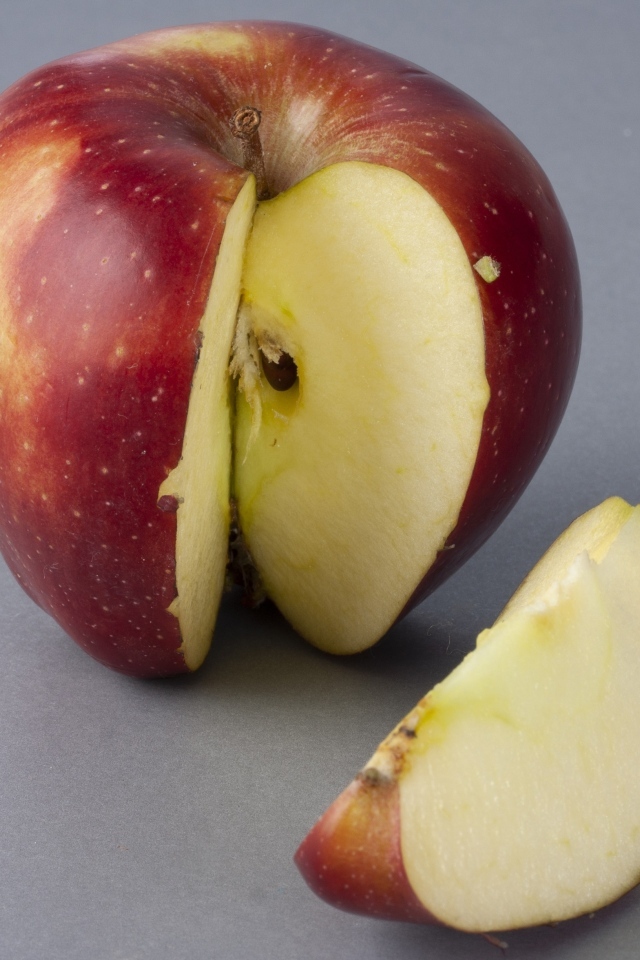 Разрезанное красное яблоко на сером фоне