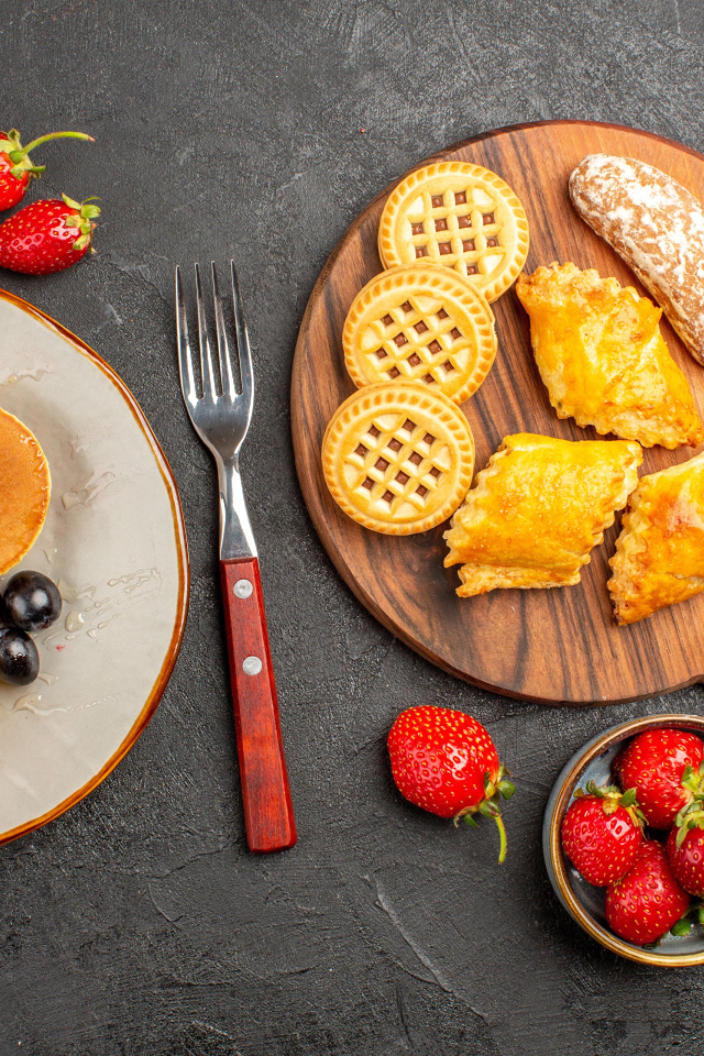 Печенье и оладьи на столе с ягодами клубники и виноградом