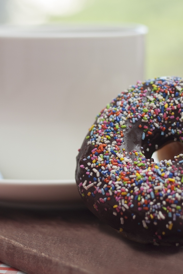 Донат с шоколадной глазурью и сладкой посыпкой на столе с чашкой чая