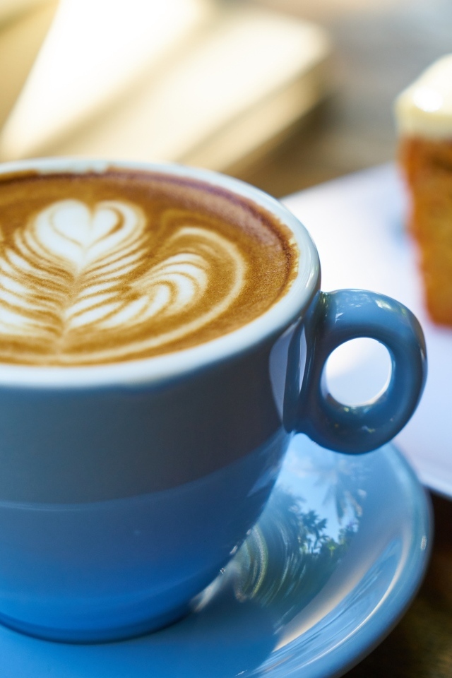 Чашка ароматного горячего кофе с рисунком на пене на столе на завтрак