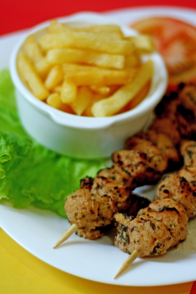 Шашлык на шпажках на столе с картофелем фри и листьями салата