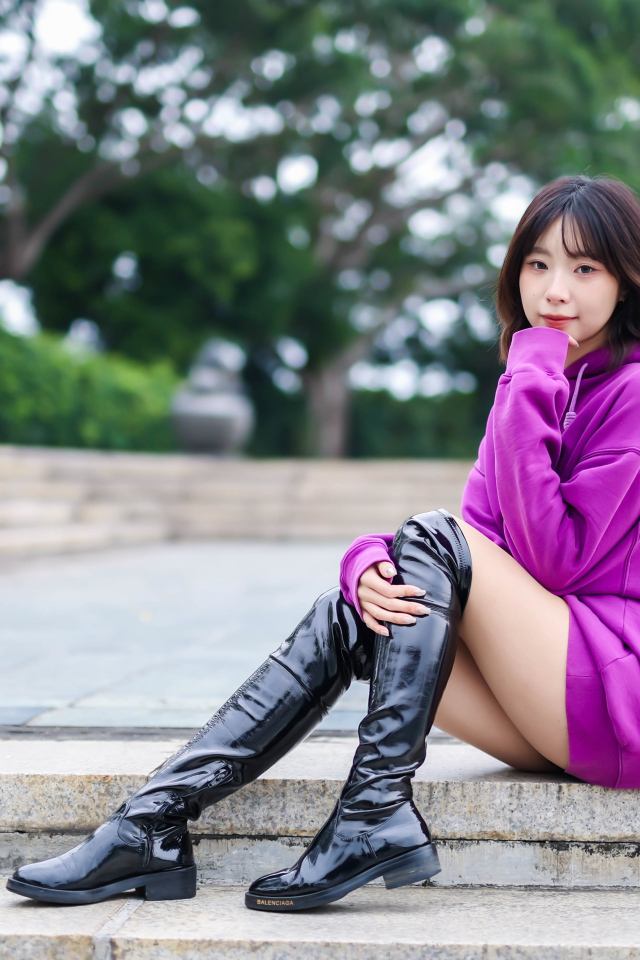 Девушка азиатка в длинных черных сапогах сидит на ступенях