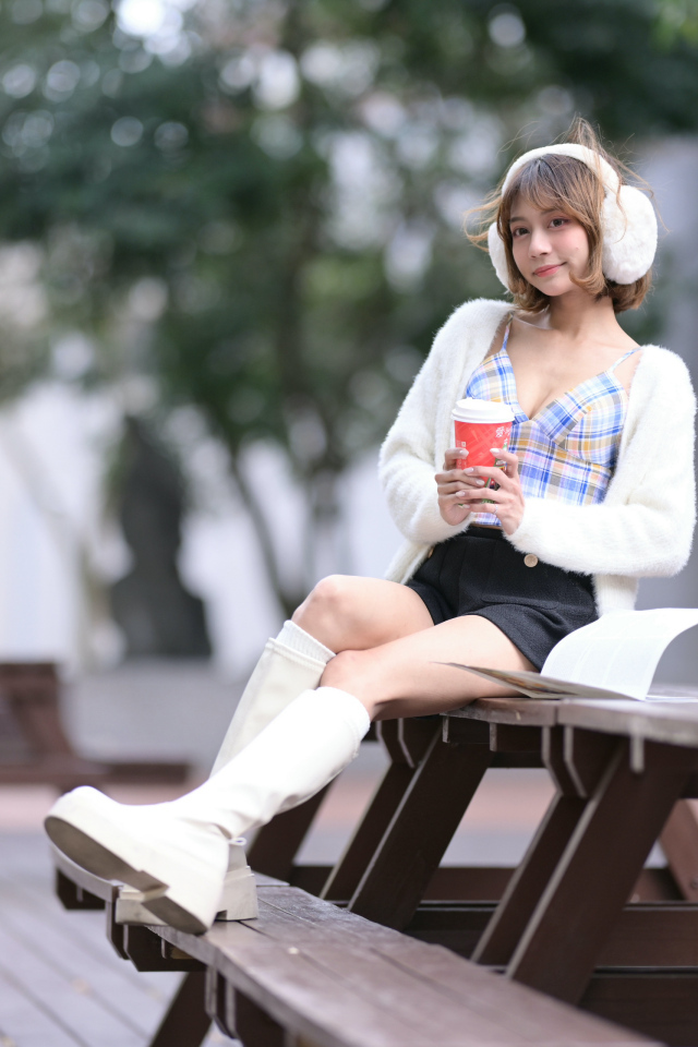 Девушка азиатка с кофе сидит на столе в парке