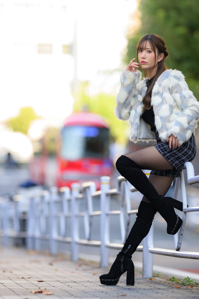 Азиатка в шубе стоит у забора