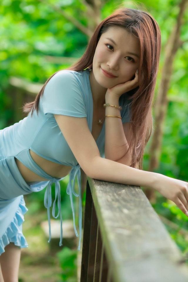 Азиатка в коротком голубом платье стоит у перил