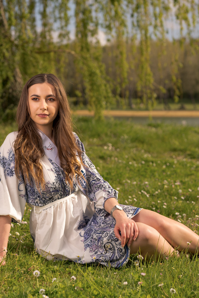 Красивая девушка в платье сидит на зеленой траве в парке