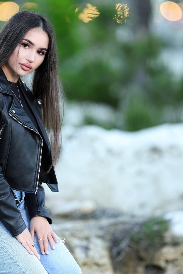 Брюнетка в черной кожаной куртке сидит на камне