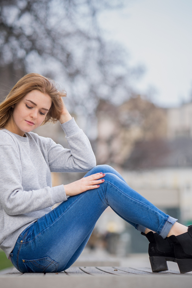 Милая девушка в синих джинсах сидит на лавке