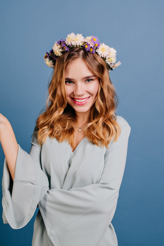 Милая улыбающаяся девушка с венком на голове на сером фоне