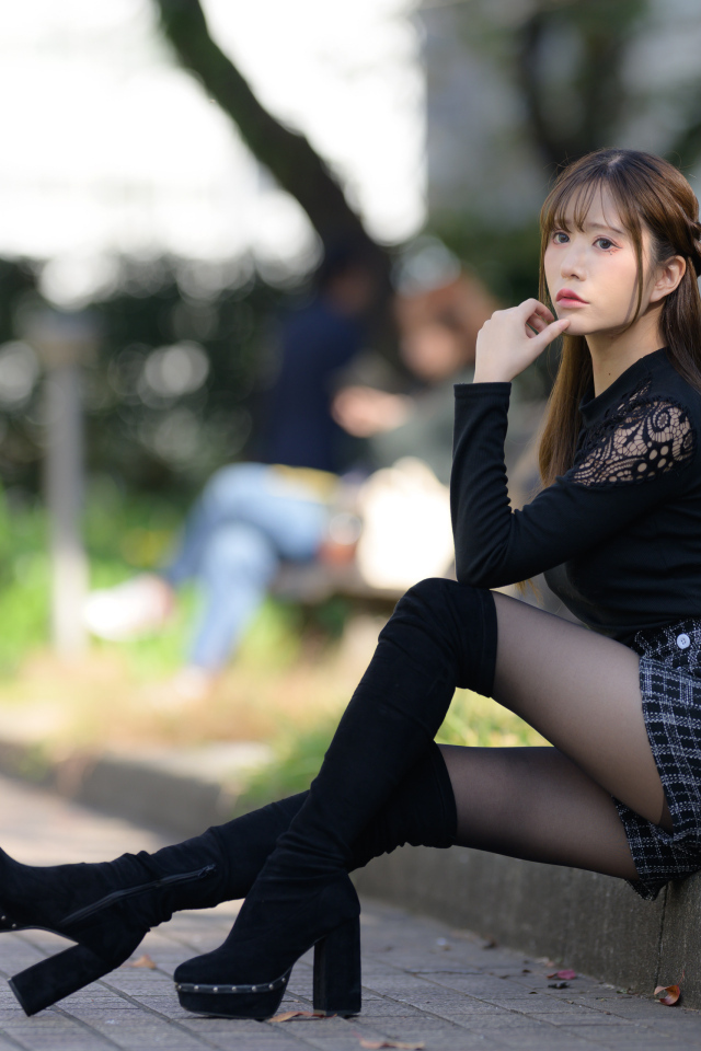 Грустная азиатка в черных сапогах сидит бордюре