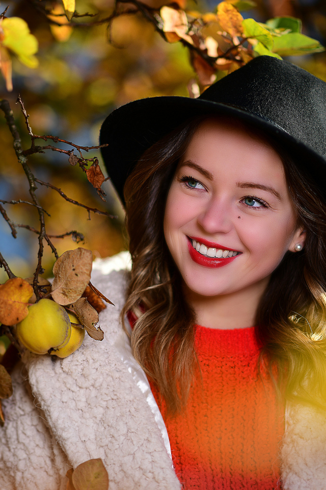 Улыбающаяся девушка в черной шляпе у дерева с яблоками