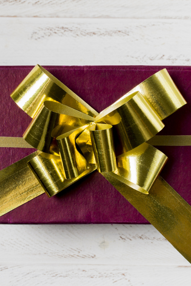 Красная коробка с подарком с золотым бантом на столе