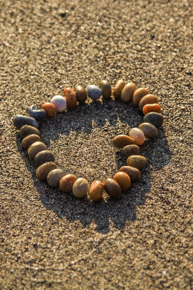 Сердце из камней на морском песке летом