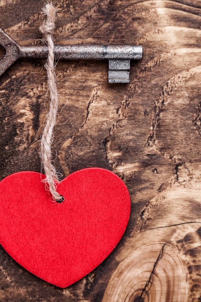 Красное сердце на нитке с ключом на деревянном фоне