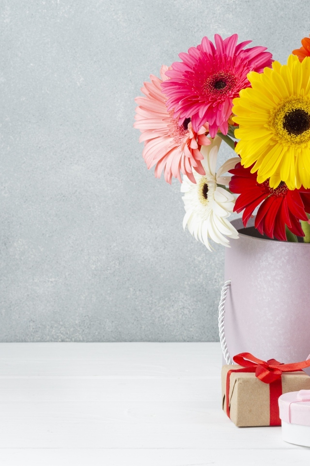 Букет разноцветных цветов герберы на столе с подарками