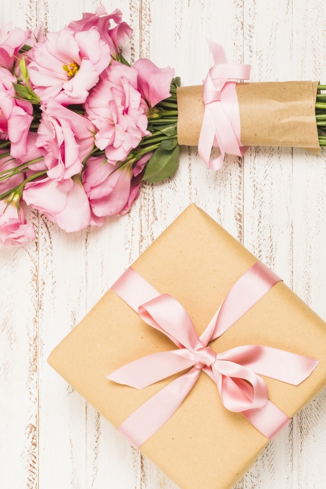 Букет розовых цветов эустомы с подарком на деревянном фоне