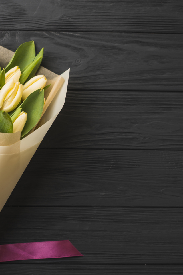 Букет желтых тюльпанов в бумаге на черном столе