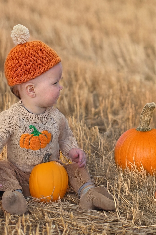 Маленький ребенок сидит на поле с тыквами