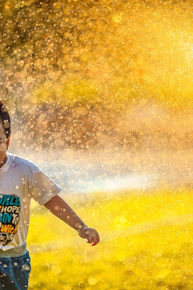 Веселый ребенок играет под брызгами воды