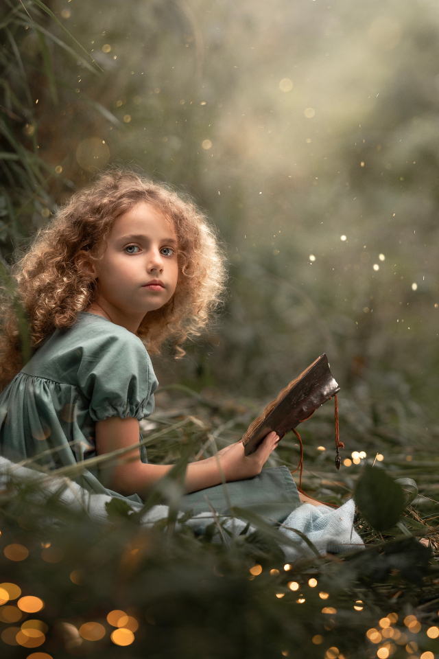 Милая девочка читает книгу сидя на траве