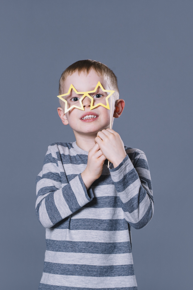 Маленький мальчик с очками в форме звезд на сером фоне