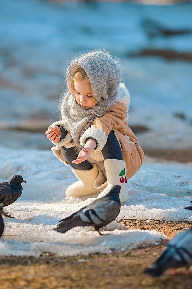 Маленькая девочка кормит голубей зимой