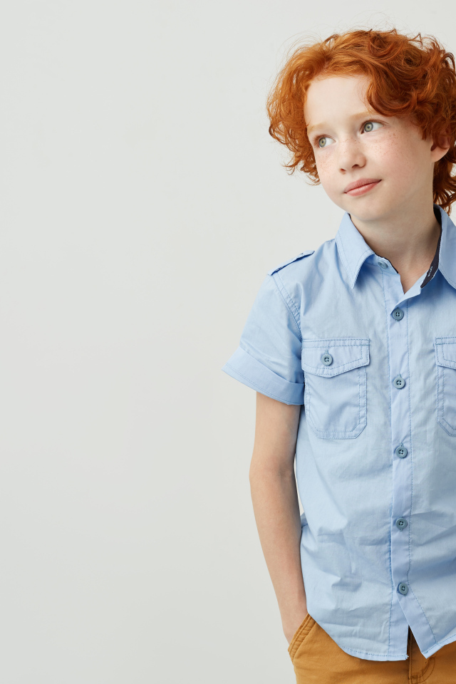 Рыжеволосый мальчик на фоне серой стены