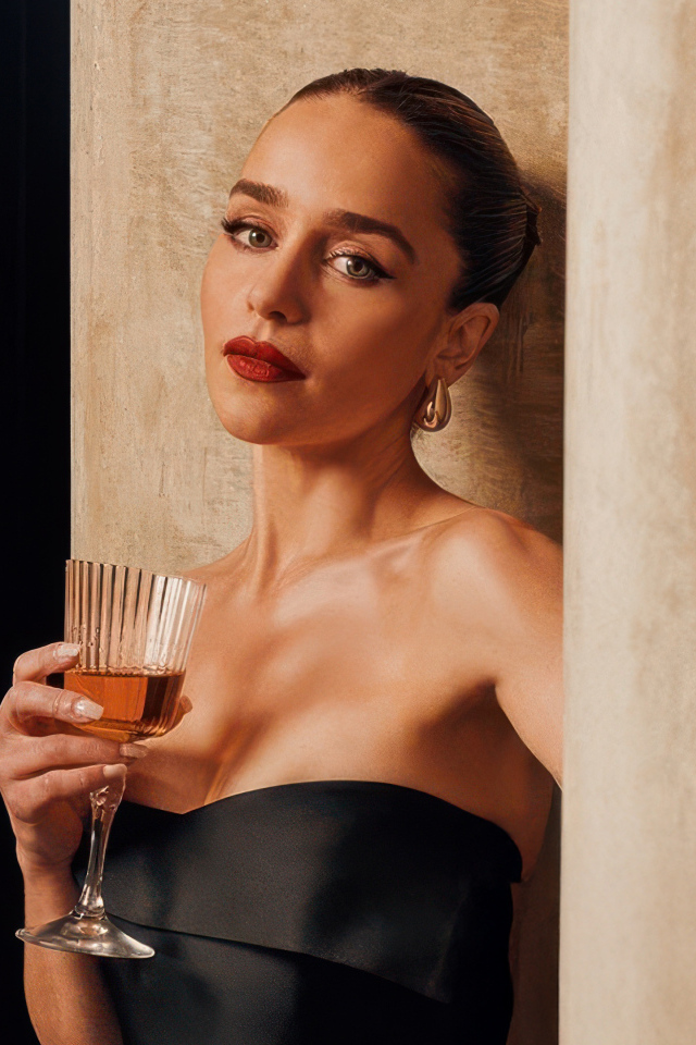 Актриса Эмилия Кларк с бокалом стоит у стены