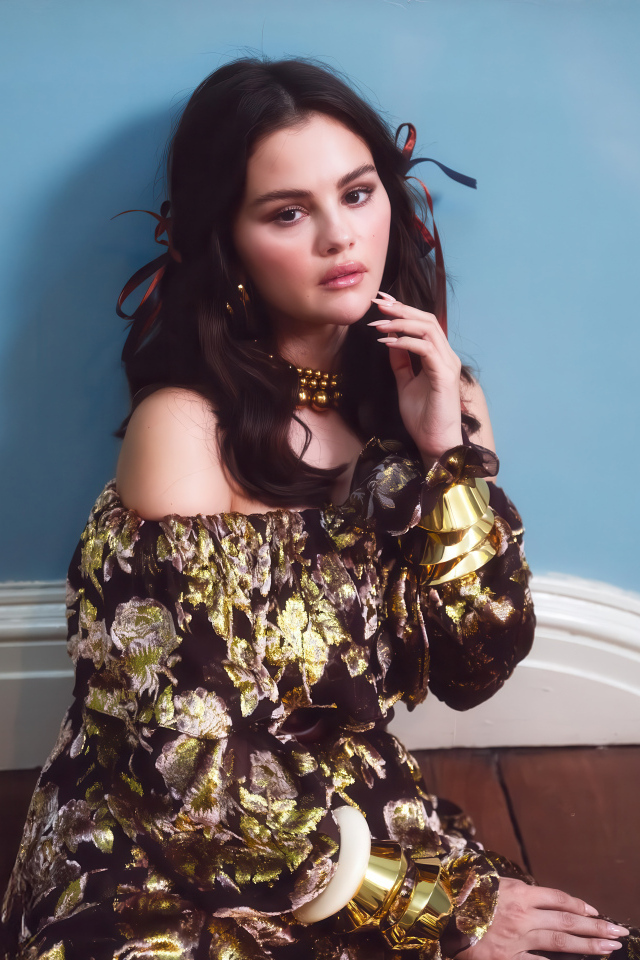 Актриса Селена Гомес на диване на фоне серой стены