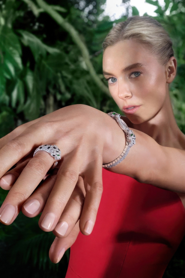 Актриса Ванесса Кирби в красном платье с кольцом на руке на фоне зарослей