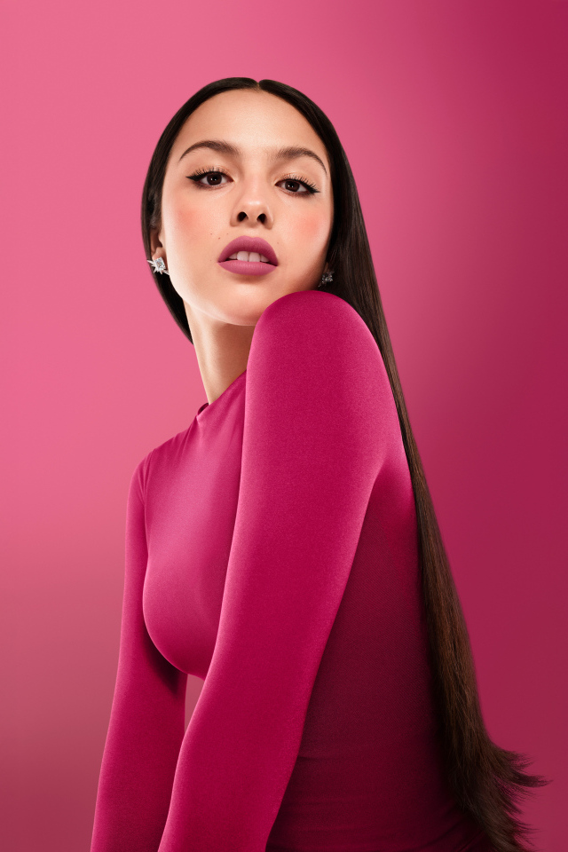 Длинноволосая актриса Оливия Родриго на розовом фоне