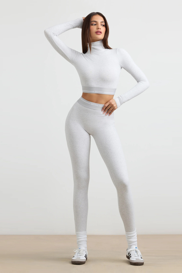 Стройная спортивная девушка в костюме позирует на сером фоне