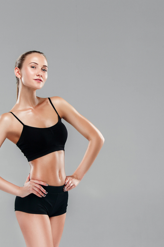 Стройная спортивная девушка в черном наряде на сером фоне