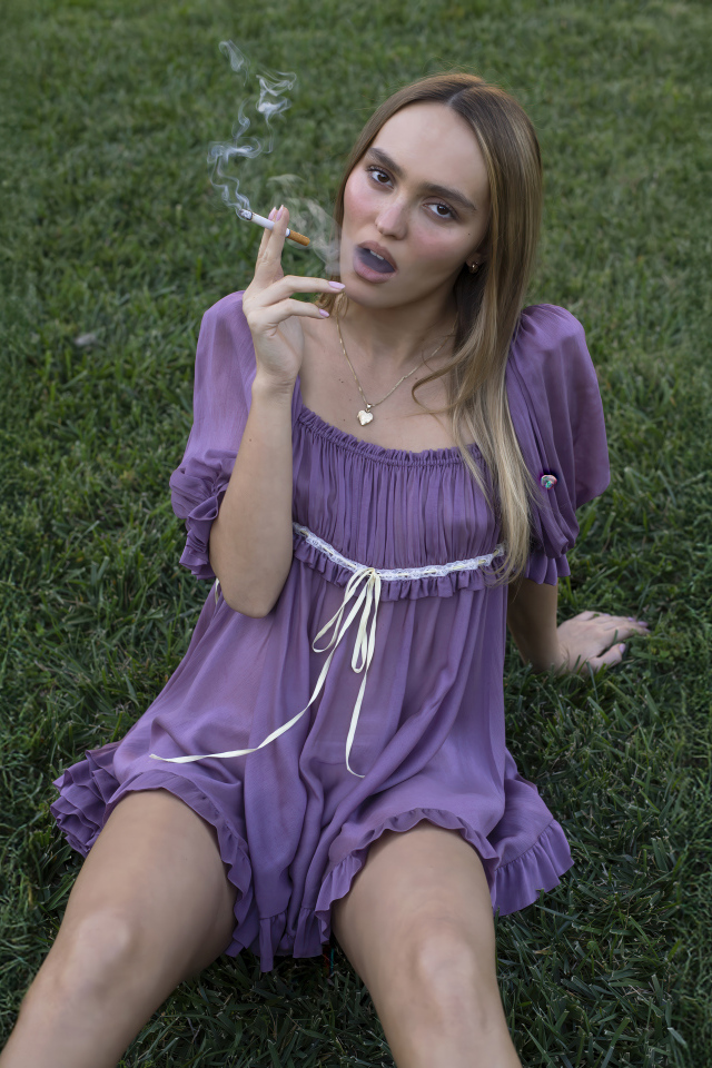 Молодая Лили-Роуз Депп с сигаретой сидит на траве